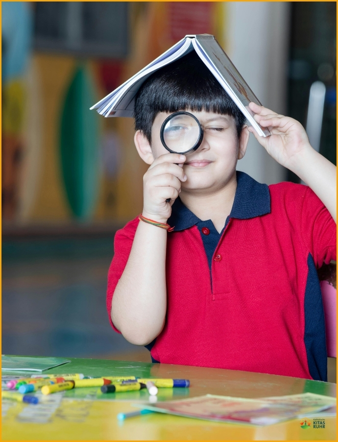 Kind mit Lupe in der Hand und Buch auf dem Kopf